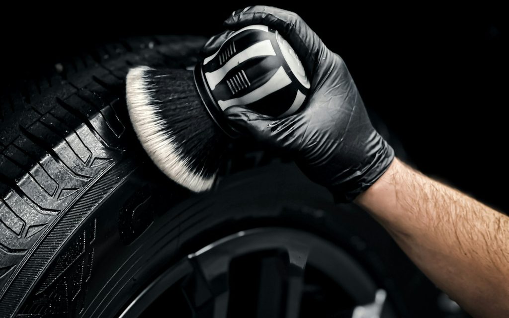 A gloved hand cleaning an alloy wheel and tyre