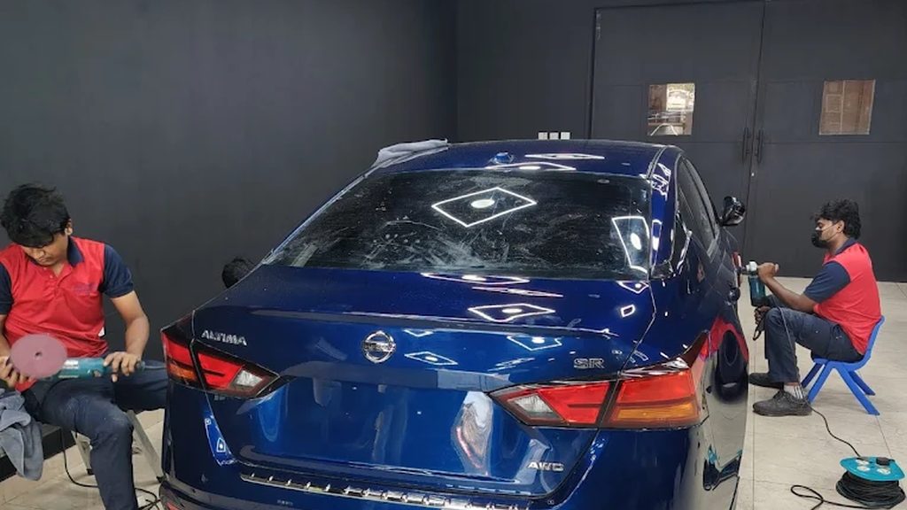Peeyesyem technicians machine-polishing a car under inspection lighting in the Deira studio