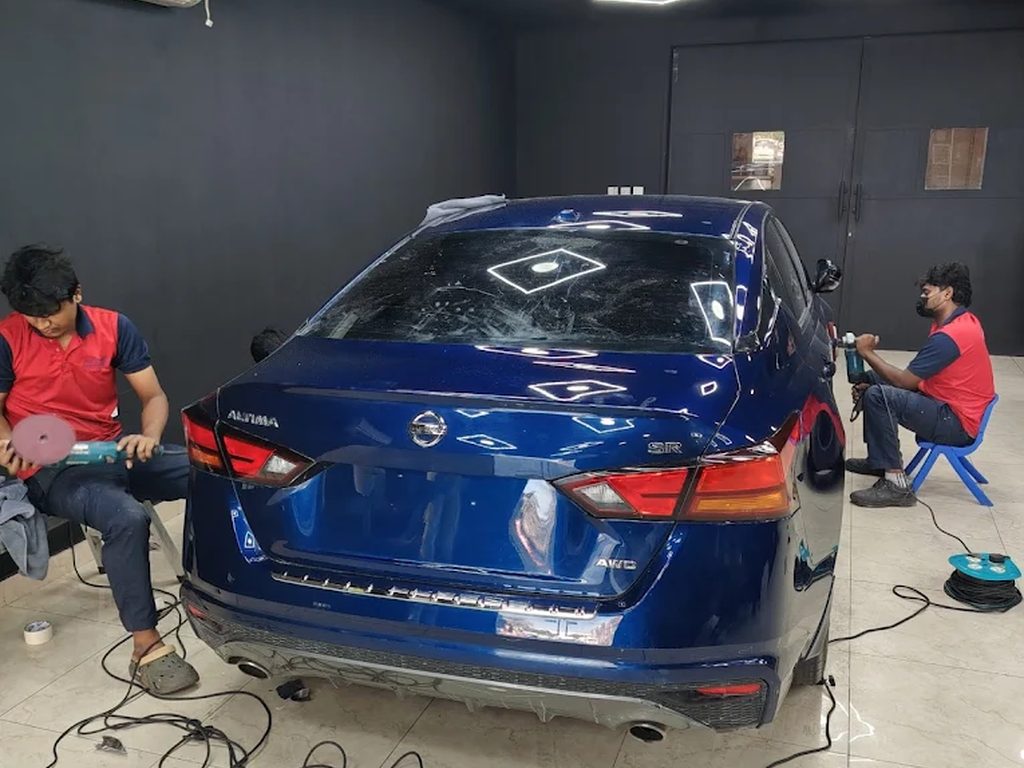 Two Peeyesyem technicians polishing a sedan in the detailing bay
